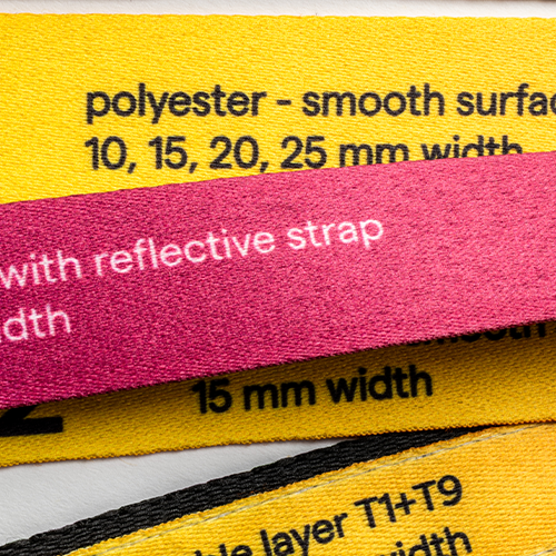 Zbliżenie na próbki taśm smyczy reklamowych o różnych szerokościach od 10mm do 25mm oraz z paskiem odblaskowym.