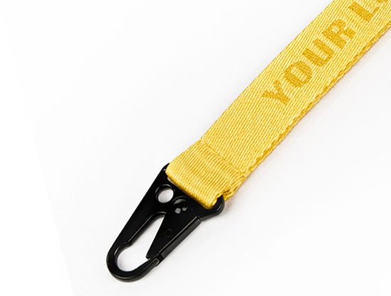 Zbliżenie na czarny metalowy karabińczyk zamontowany przy żółtej smyczy reklamowej z własnym nadrukiem.
