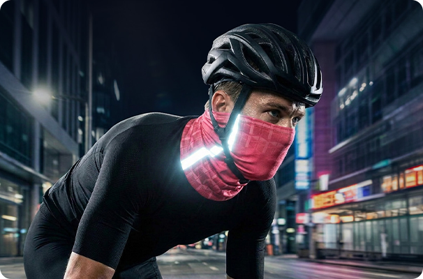 Radfahrer mit Helm und rosa reflektierendem Schlauchtuch mit Logo bei Nachtfahrten in der Stadt. 